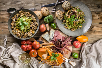 Pasta Pesto with meat and mushrooms, a variety of cheeses, smoked meat and sausage, vegetables and spicy herbs on a wooden table. Top view