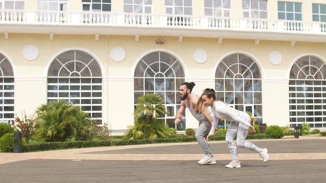 Cheerful caucasian male and female dancers performing a sportive dance on Town squre with beautiful building background.