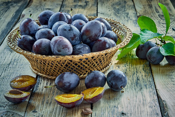 Fresh plums with leaves in basket on wooden background