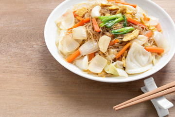 stir fried glass noodle with vegetable in a ceramic dish on wooden table, close up. asian homemade style food concept.