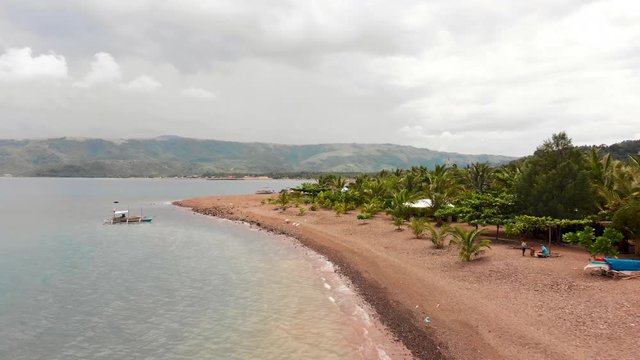Reverse drone shot on the edge of beach with beautiful island on the right and blue ocean on the left eventually revealing people swimming and playing on the beach