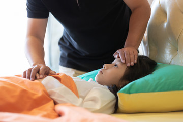 Asian girl feeling sick,female having headache and high temperature,cute little girl with father to care closely in the bedroom at home,medicine and health care concept.