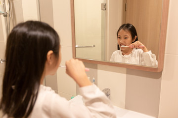 Asian girl is brushing her teeth and smiling while looking in the mirror in the bathroom