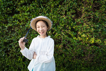 Happy girl in hat holding sunglasses,closeup of beautiful girl against greenery garden wall