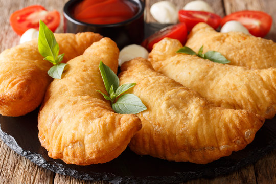 Italian fast food: fried panzerotti with tomato sauce, herbs and mozzarella close-up on a black board. horizontal