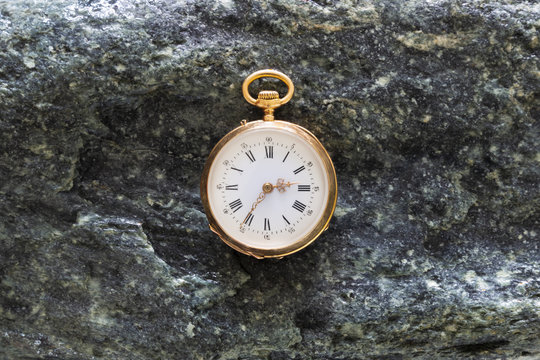 Closeup of a beautiful classic gold pocket watch laying on wet green stones