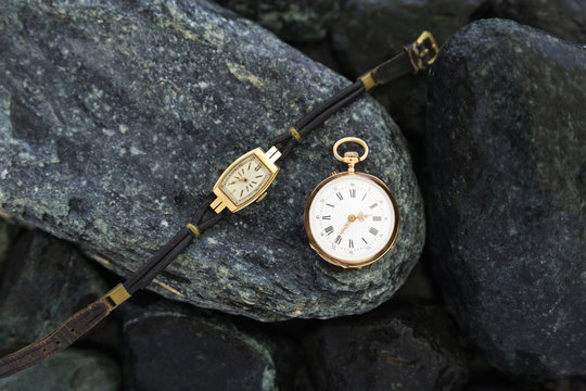 Set of watches on wet green stones with a classic gold pocket watch and a wristwatch with worn leather straps