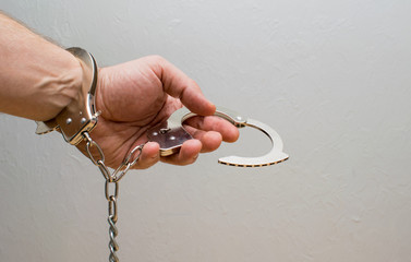 A man's hand holds handcuffs.