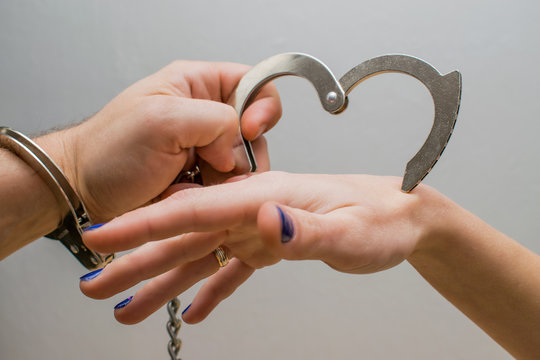The man's hand puts the handcuffs on the woman's hand.