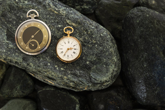 Set of watches on wet green stones with a classic gold pocket watch and a black and silver pocket watch