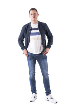 Cool Young Adult Relaxed Guy In Bomber Jacket Posing With Hands In Pockets Looking At Camera. Full Body Isolated On White Background. 