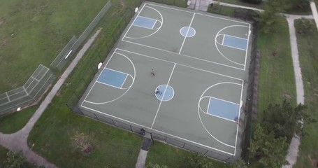 AERIAL: A tracking Shot of a Basketball Court with two teenagers riding bicycles.