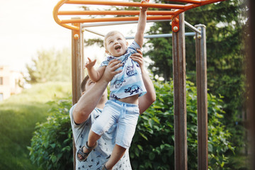 Young father and a blond boy in blue T-shirts climb the stairs at the children's playground in the summer.