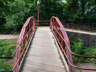 Narrow wooden bridge with red steel guards leading to footpath around canal area