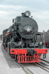 Fototapeta premium Czarny zabytkowy lokomotywa parowa z czerwonymi kołami na kolei.