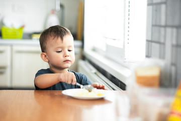 The little boy in the kitchen eagerly eating rice with a spoon independently