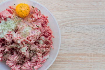 Minced meat in a bowl with raw egg, spices and chopped onion for cooking cutlets, selective focus