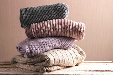 A pile of warm sweaters on a wooden table on a light background. Autumn and winter clothes.