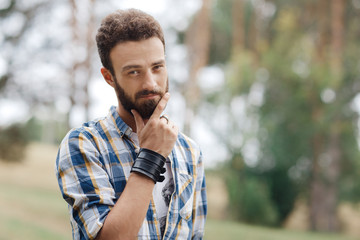 Attractive curious young bearded hipster posing in the park.