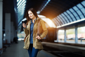 Beautiful young woman using smart-phone while standing on the railway station platform.