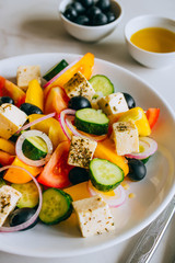 Greek salad of fresh cucumber, tomato, sweet pepper, red onion, feta cheese and olives with olive oil on marble.
