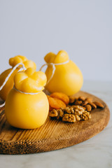 Scamorza cheese with walnuts, almonds and dried apricots on a wooden board, marble background, copy space.