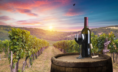 Red wine bottle and wine glass on wodden barrel. Beautiful Tuscany background