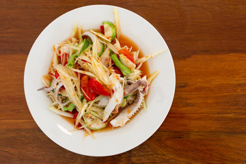 A dish of Papaya salad seafood  with Squid and Shrimp. Put on wooden table. This is  thai food of people Northeast (Esann) Thailand.  Top view.