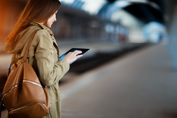 Fototapeta premium Young woman with backpack using tablet while standing on the railway station platform.