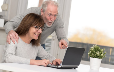 Happy mature couple having a good surprise on laptop