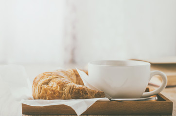 Close up of coffee cup with croissant on wooden table with vintage tone