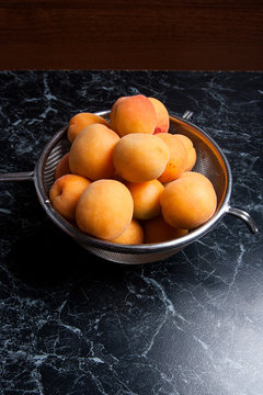 Several of harvested apricots whole and halved in steel colander..