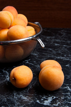 Fresh organic apricots in steel colander. Group of harvested apricots whole and halved in steel colander..