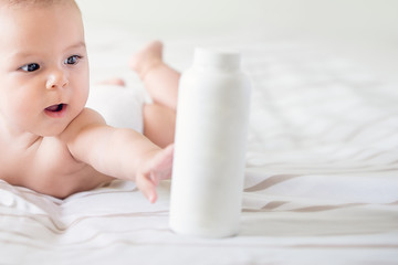 beautiful baby holding a bottle in the hand with care lotion tummy time on the bright bed airy isolated with copy space childhood medicine care
