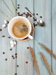A cup of coffee with sugar, coffee spoon and spikelets on a soft blue painted wooden background. Flat lay photo of morning coffee in the village