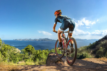 Fototapeta premium Cross-Country biker on stone trail near the lake. Male cyclist rides the rock