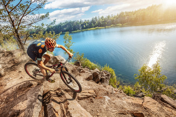 Cross-Country biker on stone trail near the lake. Male cyclist rides the rock
