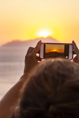 Woman taking photos of a sunset wit a mobile phone