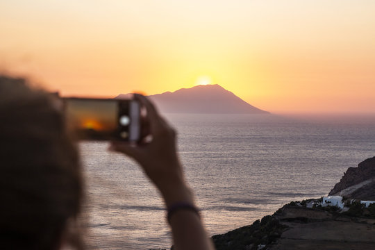 Woman taking photos of a sunset wit a mobile phone