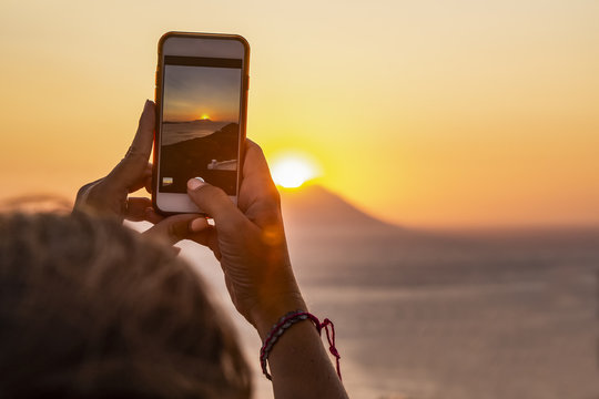Woman taking photos of a sunset wit a mobile phone