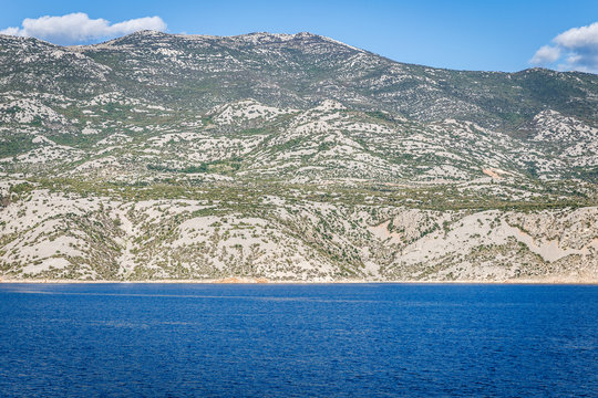 sunny day, a natural landscape with blue sea waters, blue sky and large white mountains overgrown with green shrubs and trees