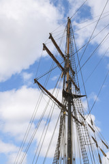Obraz premium masts and rigging of a historic sailing ship against the cloudy sky, travel and voyage concept with copy space, vertical