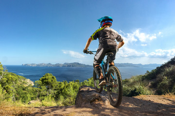 Fototapeta na wymiar Mountain biker on forest trail near the lake. Male cyclist rides the rock