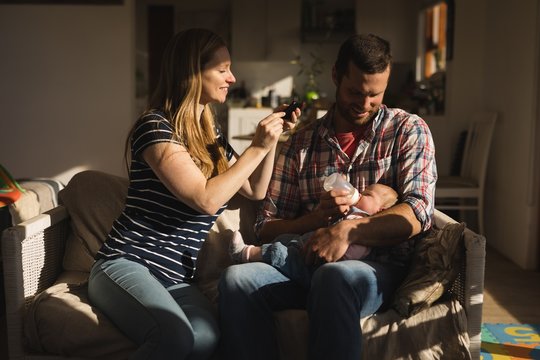 Mother taking photo from mobile while father feeding his baby on - Powered by Adobe