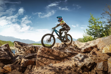 Naklejka na ściany i meble Mountain biker on stone trail. Male cyclist rides the rock