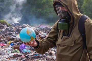 A man in a gas mask looks at the once beautiful planet earth. On the background of burning plastic trash. The concept of environmental problems — plastic garbage, illegal dumps, waste incineration