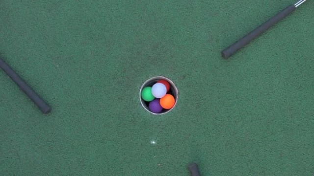 Seven Mini Golf Balls All Being Hit into the Hole at the Same Time