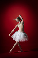 Fototapeta premium Young graceful female ballet dancer or classic ballerina dancing at red studio. Caucasian model on pointe shoes