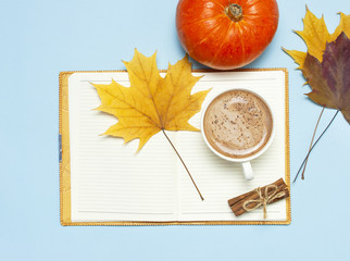 Opened notebook, orange pumpkin, pumpkin spiced latte or coffee in cup, cinnamon, yellow autumn maple leaf on blue background top view flat lay. Autumn or winter hot drink, halloween concept.