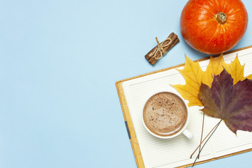 Opened notebook, orange pumpkin, pumpkin spiced latte or coffee in cup, cinnamon, yellow autumn maple leaf on blue background top view flat lay. Autumn or winter hot drink, halloween concept.